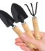 Three wooden-handled garden tools: spade, shovel, and rake, held together in a hand against a blurred background.